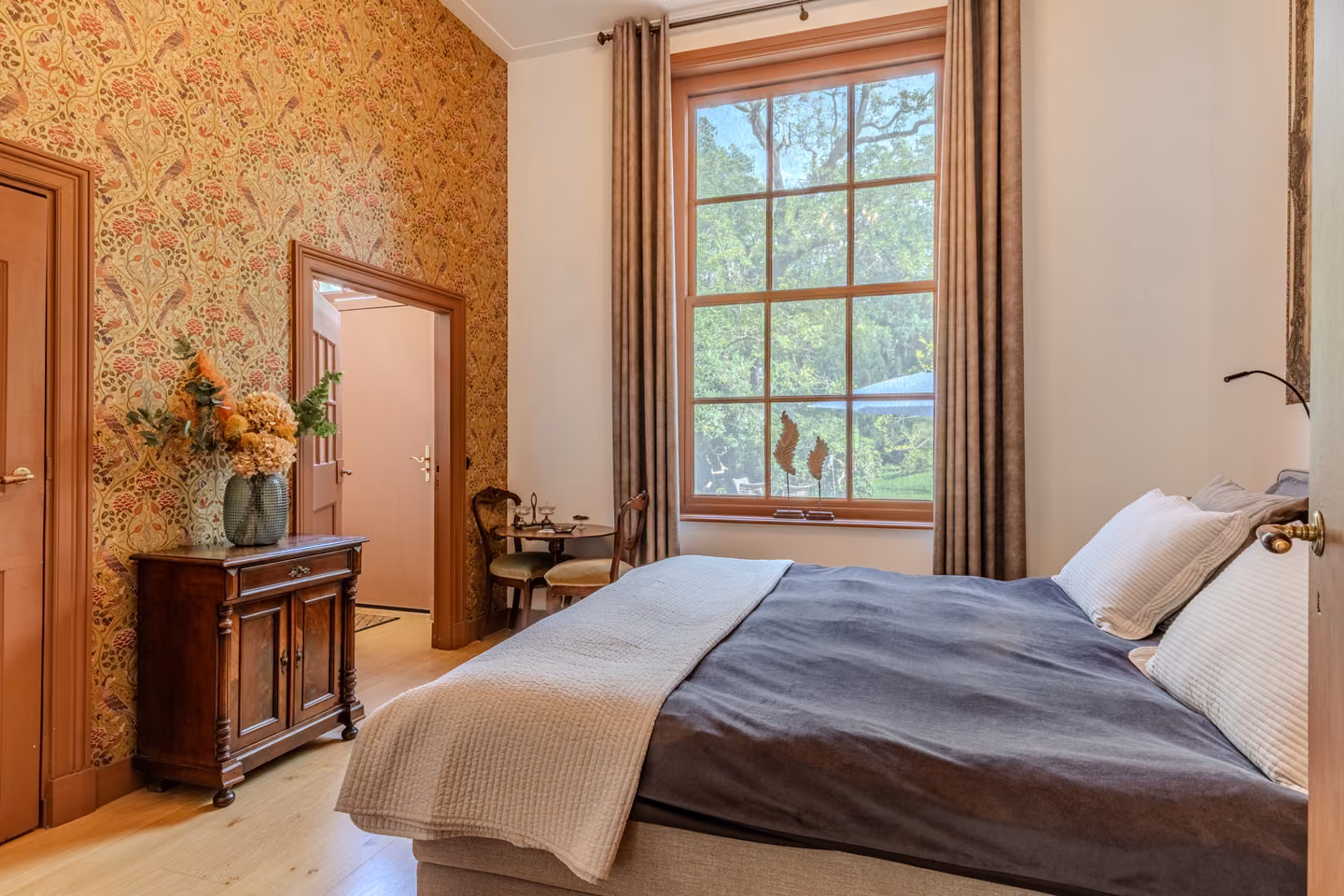 Slaapkamer met bloemenbehang en uitzicht door het hoge raam