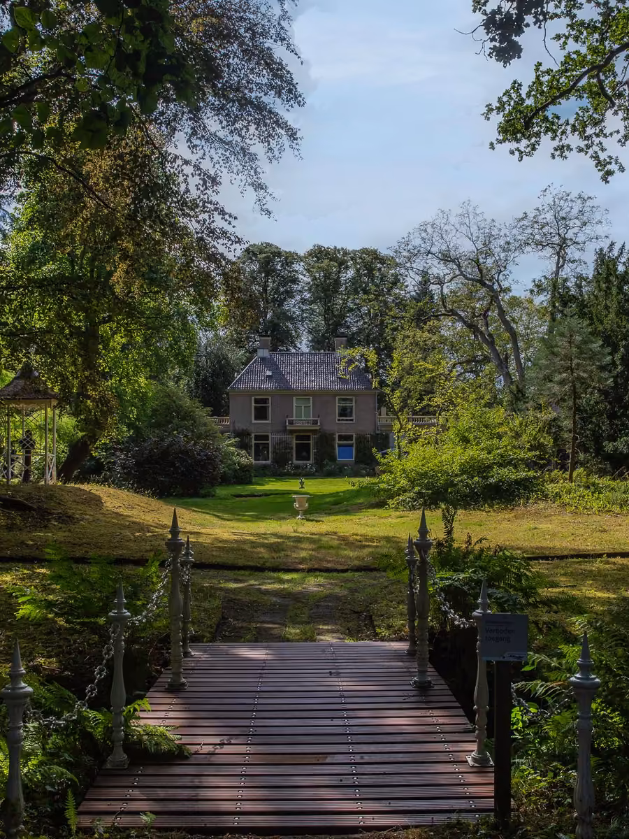 Witte houten brug in de tuin van Huis Overcingel met zicht op het huis