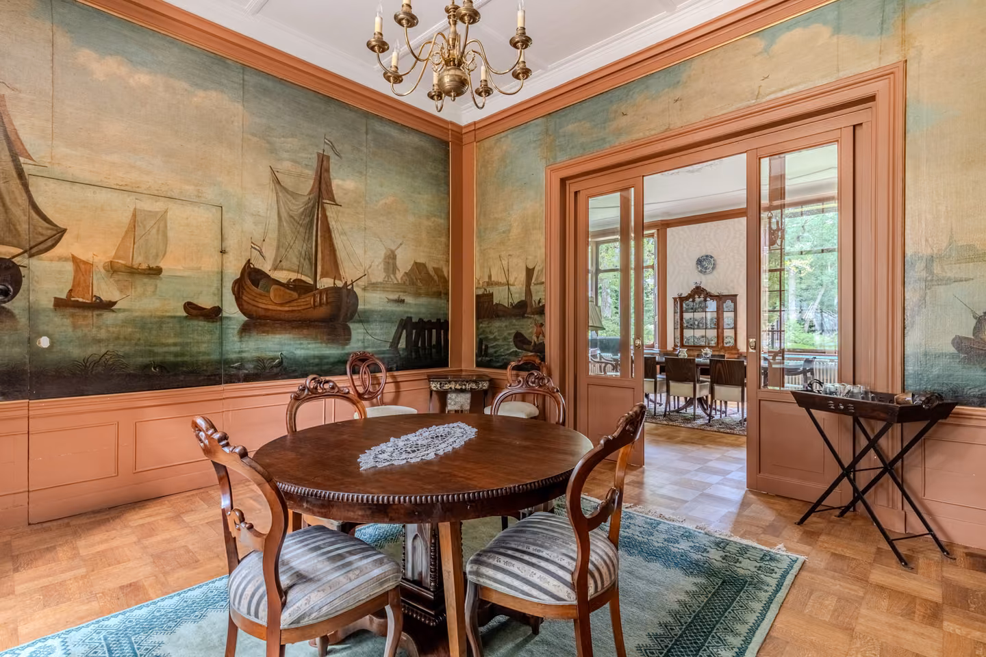 Ronde vergadertafel in de studeerkamer onder een geschilderd scheepstafereel