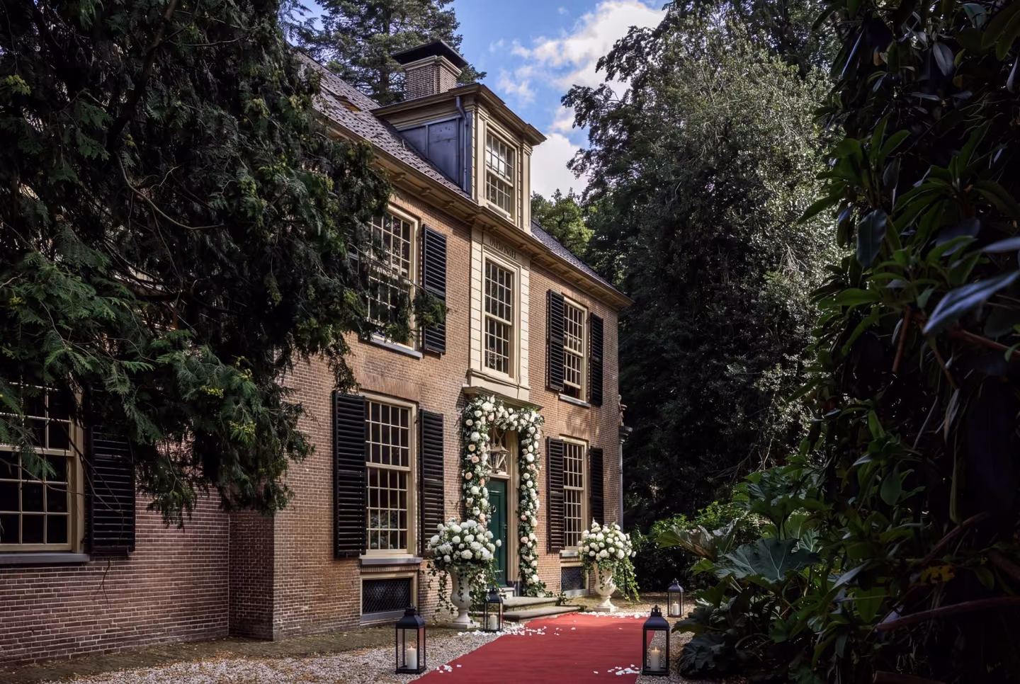 Voordeur van Huis Overcingel met bloemenboog, rode loper en lantaarns voor een bruiloft
