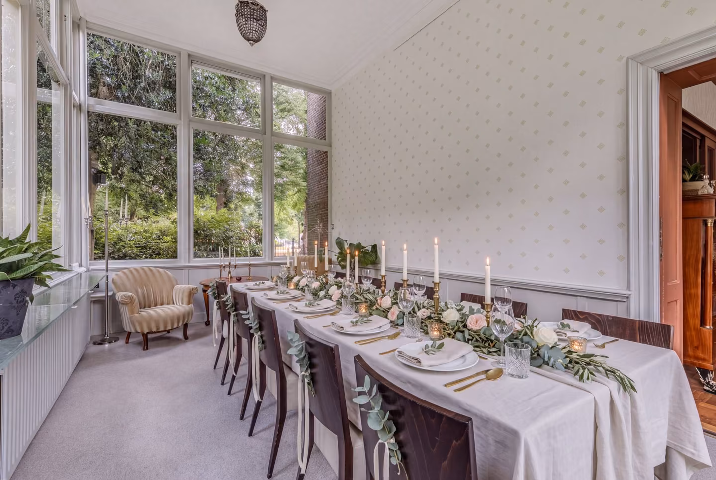 Lange gedekte tafel met kaarsen en bloemen voor een bruiloftsdiner in de tuinkamer
