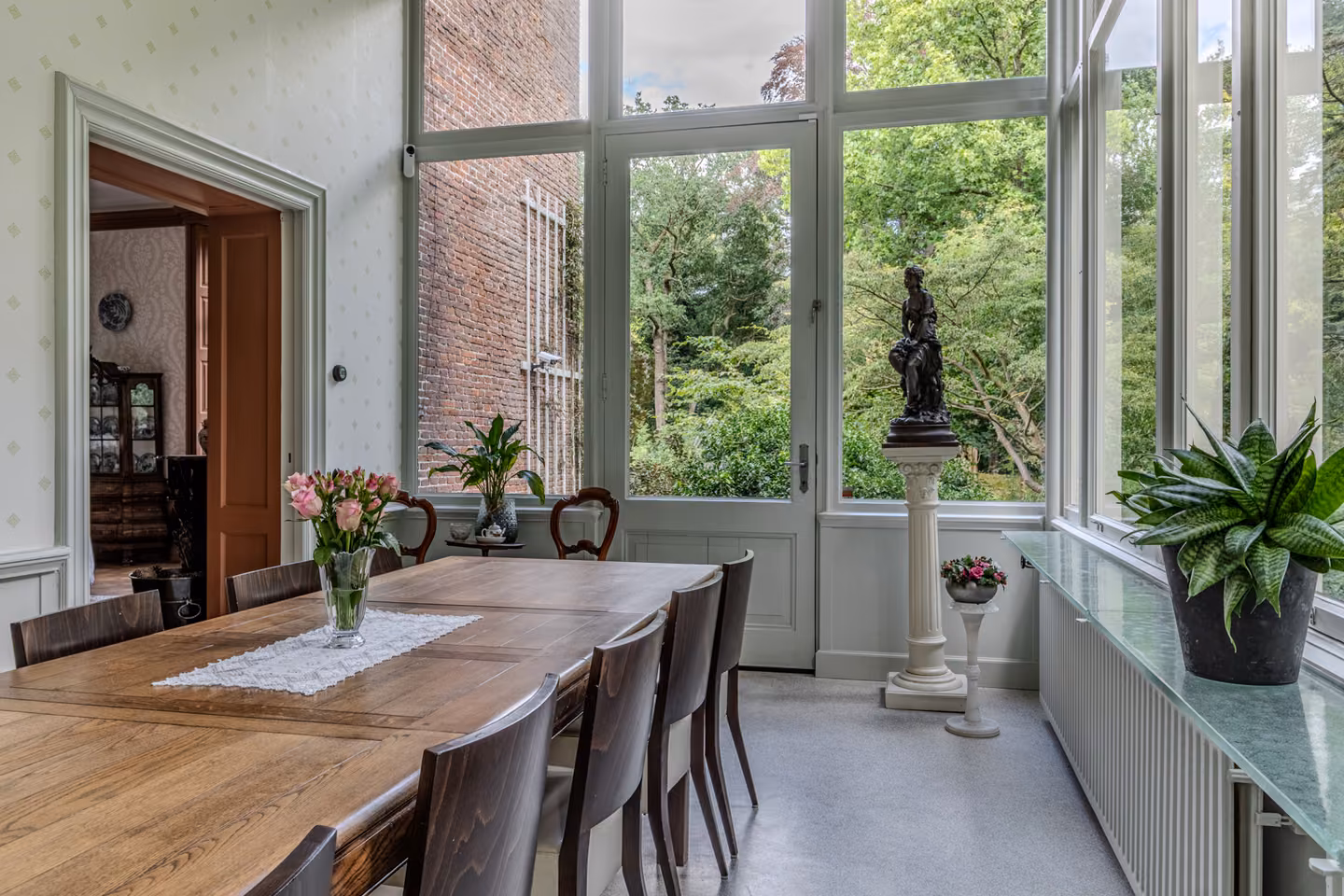 Tuinkamer met tafel, beeld en glazen deuren naar de tuin